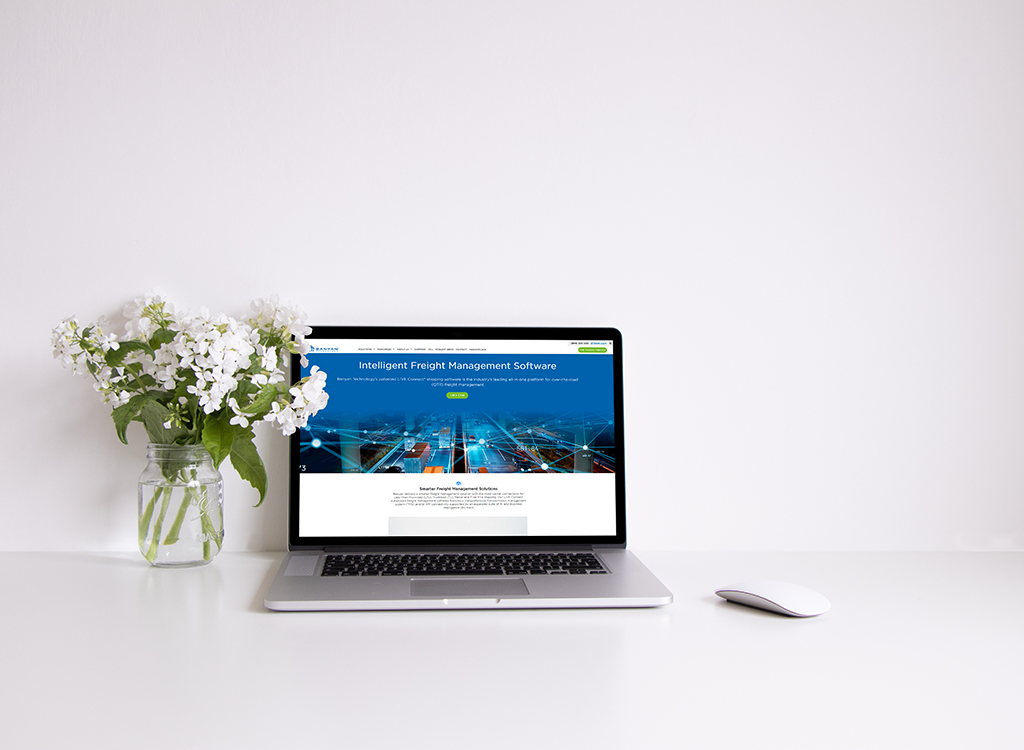 Laptop displaying an Intelligent Freight Management Software webpage, placed on a clean desk with a white background and a vase of white flowers.