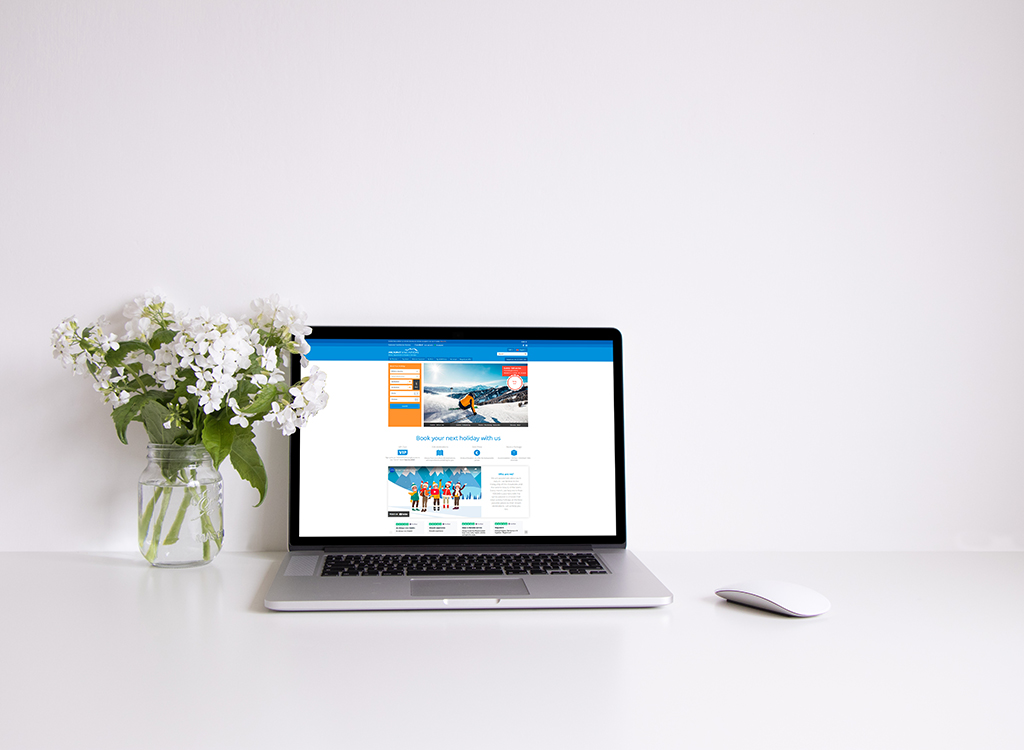 Laptop displaying a travel booking website on a clean desk, accompanied by a vase of white flowers, emphasizing a modern workspace aesthetic.